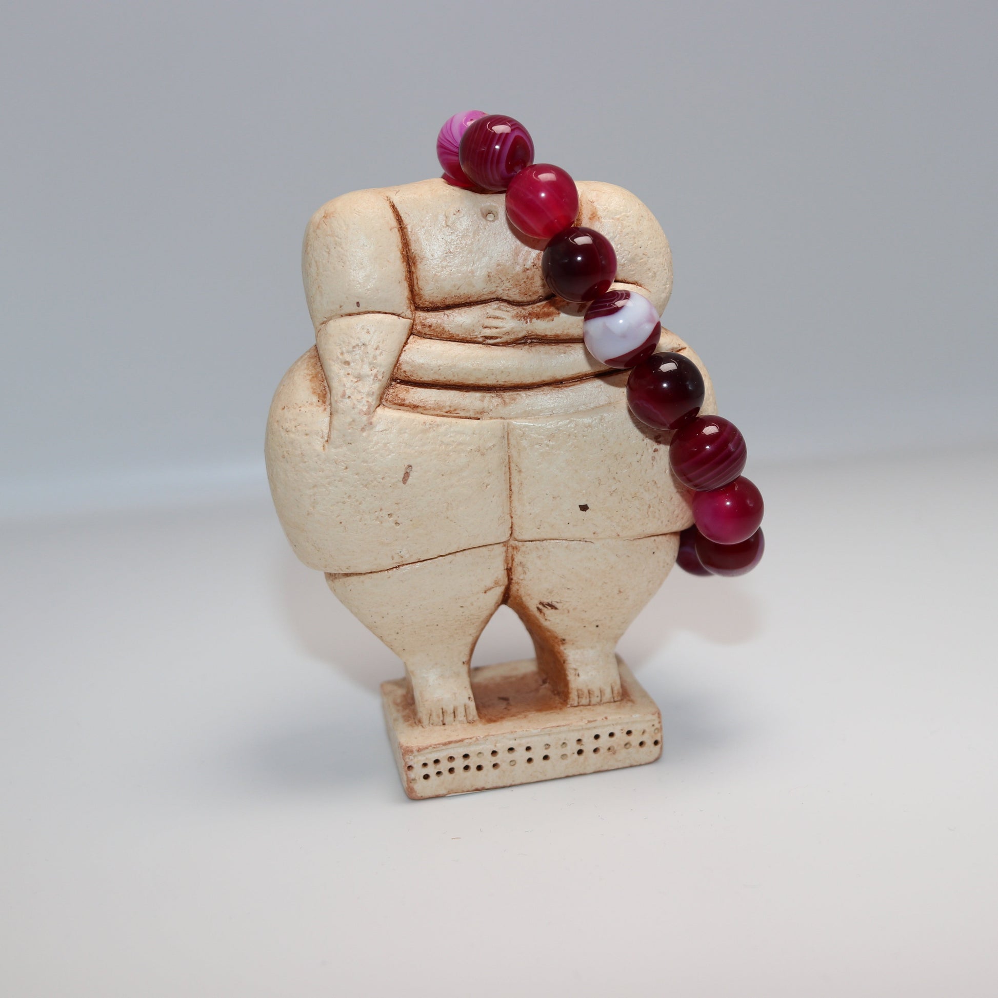 Decorative item with a beige figure and red beads on a white background